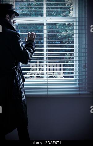Mann in Mantel und Hut spähende Fensterläden Stockfoto