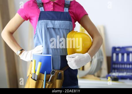 Frau in Bau Overalls mit Werkzeugen in der Tasche hält Schutz Helm in der Hand Stockfoto