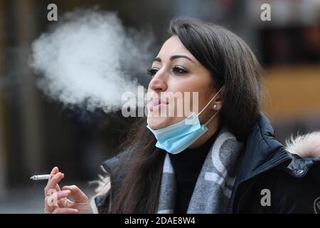 München, Deutschland. November 2020. Maskenpflicht in den Fußgängerzonen und öffentlichen Plätzen in München am 11.11.2020. Die junge Frau trägt ihre Alltagsmaske unter ihrem Gesicht und raucht eine Zigarette. MODELL FREIGEGEBEN! Quelle: dpa/Alamy Live News Stockfoto