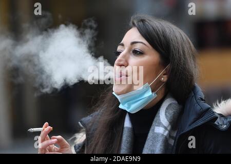 Maskenpflicht in den Fußgängerzonen und öffentlichen Plätzen in München am 11.11.2020. Die junge Frau trägt ihre Alltagsmaske unter ihrem Gesicht und raucht eine Zigarette. MODELL FREIGEGEBEN! Weltweite Nutzung Stockfoto