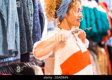Glückliche Frau testet und trägt neue Pullover für die Wintersaison In einem Geschäft - Konzept von Shopping und Verkauf - Die Leute kaufen farbige Jacken Stockfoto