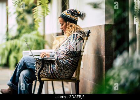 Schöne junge Dame arbeiten mit Computer Laptop im Freien sitzen auf Eine Bank mit grünen Pflanzen im Hintergrund - Konzept Von modernen Menschen und Online-Arbeit - neue Arbeit smart Arbeitsleben Stockfoto