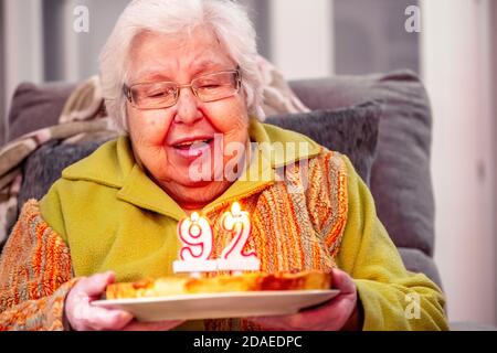 Alte Frau mit Geburtstagskuchen Kerzen ausblasen sitzen in Sessel Stockfoto