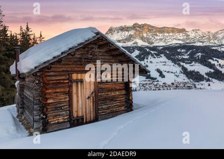 Traditionelle Holzhütte im Winter, im Hintergrund das Dorf St. Leonhard und Heiligkreuzkofel, Naturpark Fanes Sennes Prags, Abtei, Badia, Ladintal, Gadertal, Bozen, Südtirol, Italien, Europa Stockfoto