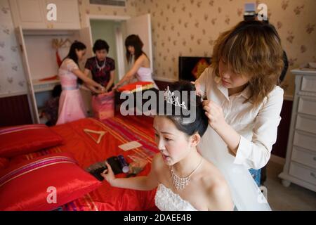 PEKING, CHINA - 2006. JUNI: Eine Make-up-Künstlerin bringt am Morgen ihrer Hochzeit den letzten Schliff an die Haare von Xie Fei, 25, einer zukünftigen Braut, während sie letzte Minuten Anweisungen an ihre Mutter und Cousins ausgibt. Stockfoto