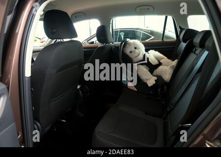 Das weiche Spielzeug sitzt in einem Kindersitz, befestigt mit einem Hundeschutzgurt, im Auto. Stockfoto