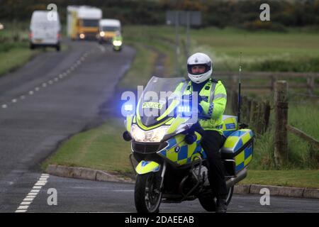 Ayrshire, Schottland, Großbritannien. Die London 2012 Olympic Fackel reist durch South Ayrshire, angefeuert von lokalen Gemeinden und Schulkindern. Die Autokolonne mit der Fackel und der Begleitmannschaft kommt mit Polizeieskorte in Maidens, Ayrshire an Stockfoto