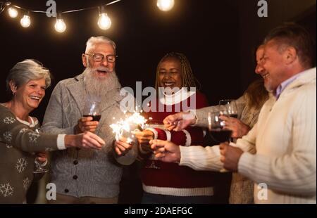 Glückliche Senioren, die Spaß haben, Feiertage zu feiern, Wein zu trinken und zu halten Wunderkerzen Feuerwerk Stockfoto