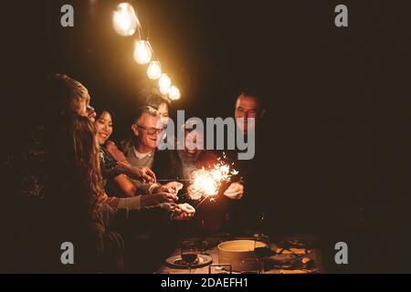 Glückliche Familie feiert Urlaub mit Wunderkerzen Feuerwerk am Abend Abendessen Party - Gruppe von Menschen mit unterschiedlichen Alters und ethnischer Zugehörigkeit Spaß haben Stockfoto