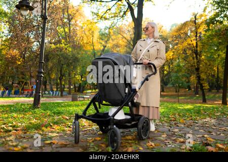 Mama mit Kinderwagen spaziert im Herbstpark Stockfoto