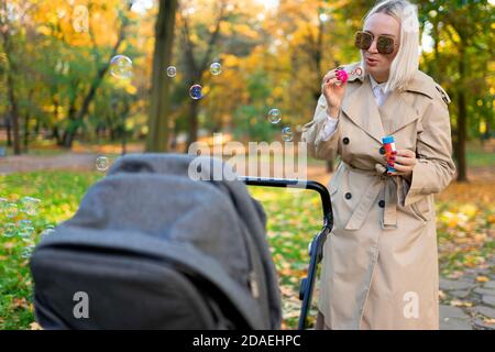 Mutter bläst Seifenblasen, um Baby im Kinderwagen zu unterhalten Stockfoto