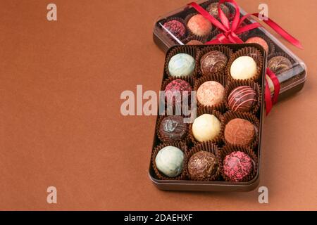 Schokolade Bonbons Trüffel Toppings Box Satin Band vor braunem Hintergrund. Stockfoto