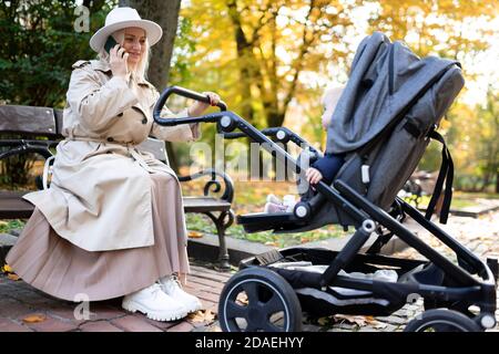 Mutter schaukelt neugeborenes Baby in einem Kinderwagen und spricht weiter Das Telefon Stockfoto