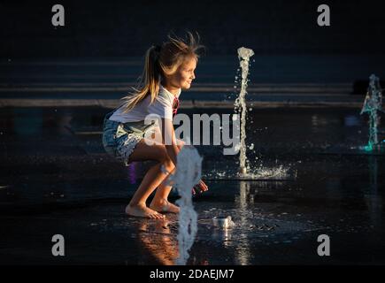 KIEW, UKRAINE - 05. Jun 2018: Fröhliches und glückliches Mädchen, das in einem Brunnen spielt und an einem heißen Tag die kühlen Wasserströme genießt. Heißer Sommer. Stockfoto