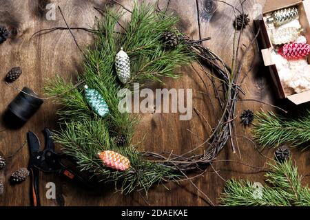 Frau macht weihnachtskranz aus Naturzweigen. Dunkler Holztisch Stockfoto