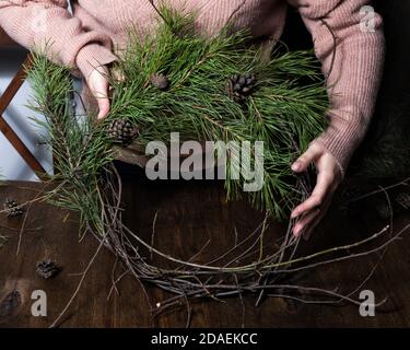 Frau macht weihnachtskranz aus Naturzweigen. Dunkler Holztisch Stockfoto