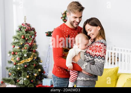 Glückliche Eltern halten in den Armen Baby Junge in der Nähe geschmückt weihnachten Baum auf unscharfem Hintergrund Stockfoto