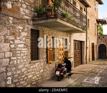Ein isolierter Roller, der im Hof eines alten Steinhauses eines mittelalterlichen italienischen Dorfes (Gubbio, Umbrien, Italien, Europa) geparkt ist Stockfoto