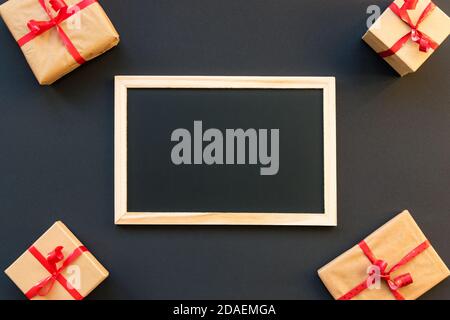 Kreidetafel auf schwarzem Hintergrund, umgeben von Geschenken. Weihnachten und Neujahr. Weihnachtseinkäufe am schwarzen freitag Konzept, Modell. Stockfoto