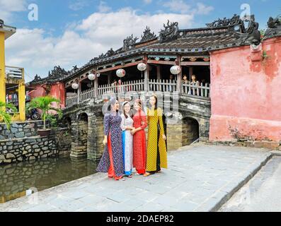 Vier vietnamesische junge Damen in traditioneller Kleidung, die Ao dai, posieren für ein Foto an der japanischen überdachten Brücke, Hoi an, Vietnam, Asien Stockfoto