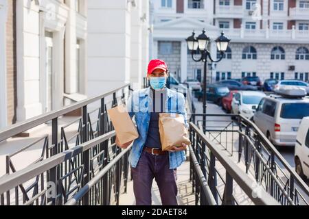 Lieferung, Post und Menschen Konzept - Mann in einer Schutzmaske Lieferung von Kaffee und Essen in Einweg-Papiertüte zum Kunden nach Hause Stockfoto