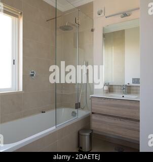 Neues Badezimmer mit Badewanne, Waschbecken und Duschabtrennwand mit beigefliesten Wänden Stockfoto