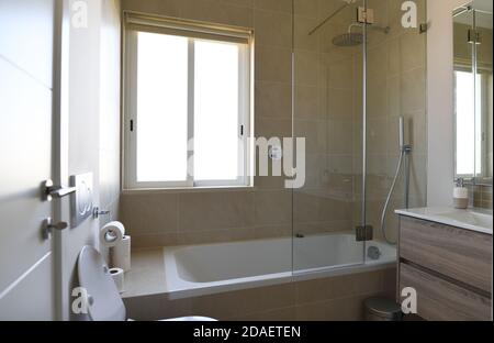 Neues Badezimmer mit Badewanne, Waschbecken und Duschabtrennwand mit beigefliesten Wänden Stockfoto