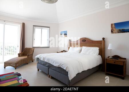 Hauptschlafzimmer mit Holzmöbeln, weißer Bettwäsche und Schiebetüren zur Terrasse in einer renovierten Ferienvilla Stockfoto