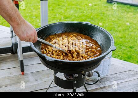 Mann Rühren Hühnerfleisch in Gusseisen Kessel im Freien. Stockfoto