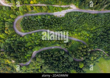 Luftaufnahme einer kurvenreichen Landstraße, die durch den grünen Wald und Berg führt. Weiße Campingwagen fahren durch. Stockfoto