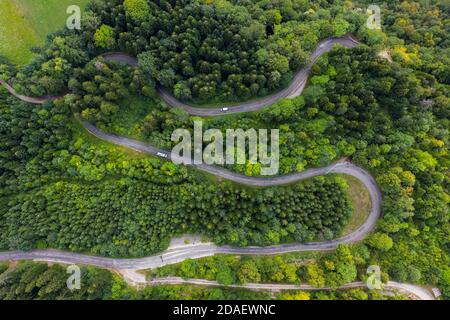 Luftaufnahme einer kurvenreichen Landstraße, die durch den grünen Wald und Berg führt. Weiße Campingwagen fahren durch. Stockfoto