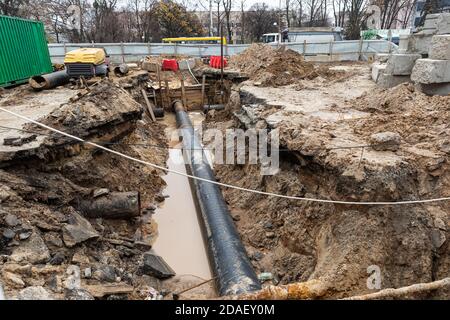 Reparatur von Straßen und unterirdischen Versorgungseinrichtungen. Der große Graben auf der Straße mit dem Rohr, der Prozess der Reparatur oder des Austauschs der Wasserleitungen in der großen Stadt. Сonstruc Stockfoto