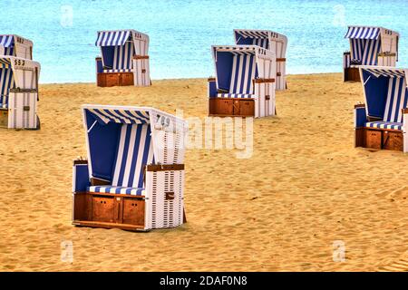Leere weiße Seilkörbe mit blau-weiß gestreiften Bezügen An einem Sandstrand mit dem Meer im Hintergrund Stockfoto
