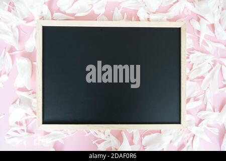 Schwarzes Brett für Notizen auf dem rosa Hintergrund mit weißen Pfingstrosenblättern. Draufsicht. Stockfoto