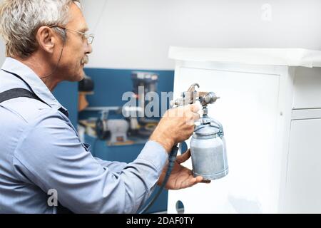 Ein Rentner mit grauen Haaren und Gläsern malt Metallprodukte. Zusätzliches Einkommen für eine ältere Person Stockfoto