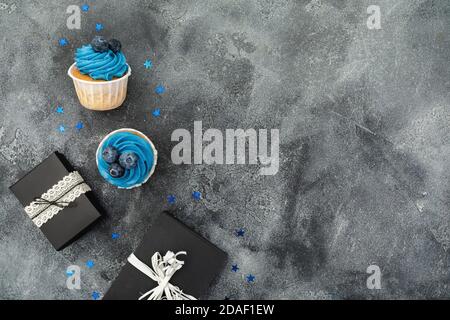 Leckere Muffins mit blauer Creme und Geschenken auf dunklem Hintergrund. Flach liegend, Draufsicht Stockfoto