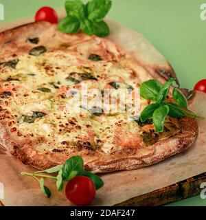 Dünne Krustenpinsa mit geräuchertem Lachs, Basilikum und Mozzarella auf grünem Hintergrund. Traditionelle italienische Küche. Nahaufnahme Stockfoto