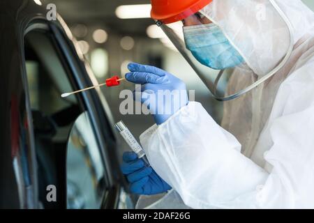 Medizinischer NHS-Arbeiter in persönlicher Schutzausrüstung, der eine Person abschabte In einem Auto fahren durch Coronavirus COVID-19 mobile Testzentrum, oral Und nasal Stockfoto