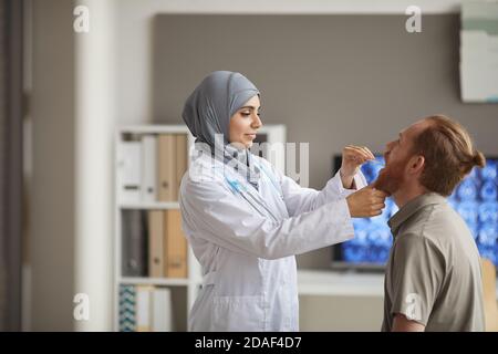 Muslimische Ärztin im weißen Mantel untersucht die Kehle Der Patient während der medizinischen Untersuchung im Krankenhaus Stockfoto