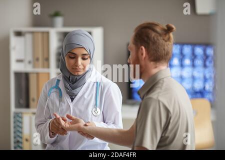 Krankenschwester in Hijab Untersuchung des Pulses des Patienten während der medizinischen Untersuchung während er die Arztpraxis besucht Stockfoto