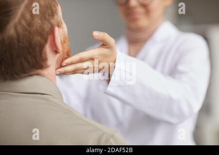Rückansicht des männlichen Patienten, der beim Besuch im Krankenhaus sitzt Während der Arzt seine Kehle untersucht Stockfoto