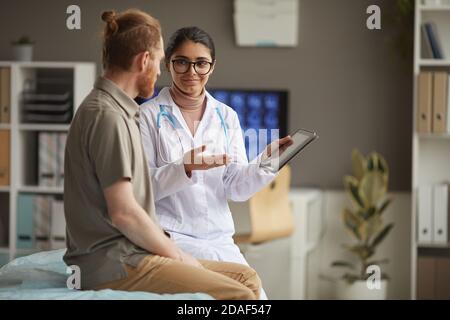Junge Krankenschwester im weißen Mantel zeigt medizinische Rezept auf digital Tablette und Gespräch mit dem Patienten während seines Besuchs bei Krankenhaus Stockfoto