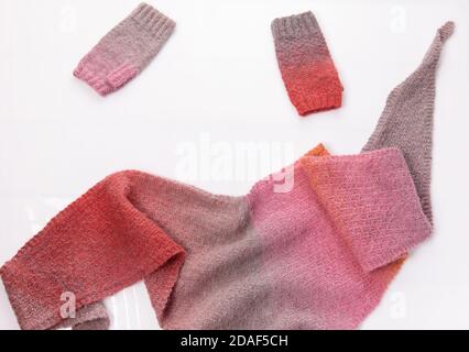 Wollgestricktes Tuch und graue und rosa Wollhandschuh auf weißem Hintergrund. Stockfoto