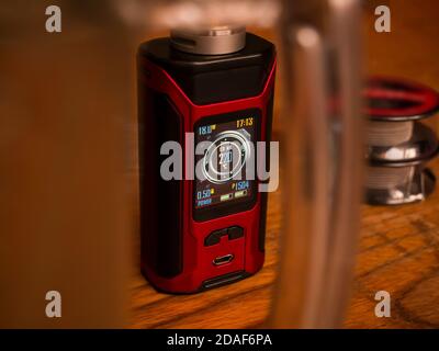 Elektronischer Dampfmod auf einem Holztisch - Blick durch den Glashalter des Glases. Im Hintergrund eine Drahtspulen für die Bildung von Heizspulen. Stockfoto