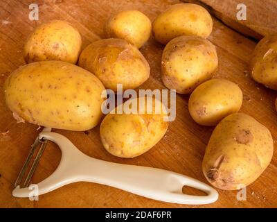 Neue Kartoffeln und weißer Schäler auf einer hölzernen Arbeitsplatte Stockfoto