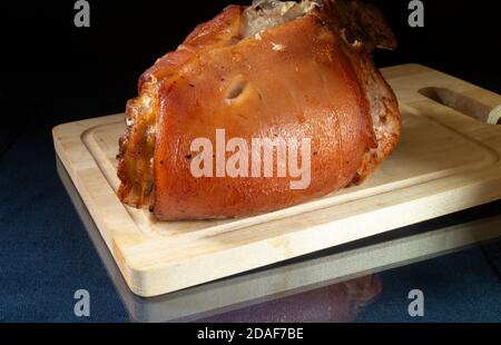 Das gebratene Bein des Schweins auf Holzbrett. Stück Fleisch auf schwarzem Hintergrund Stockfoto