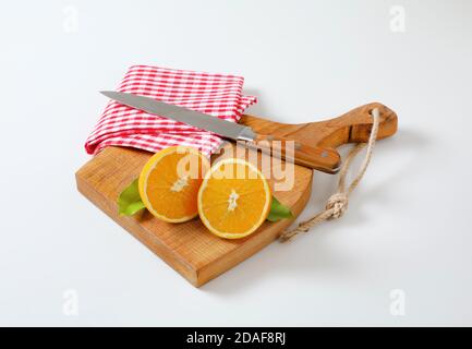 Halbierte frische Orange, scharfes Küchenmesser und Geschirrtuch auf Schneidebrett Stockfoto