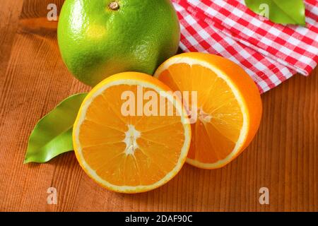 Grüne Grapefruit (Sweetie, Pomelit, Oroblanco), zwei orangefarbene Hälften und kariertes rot-weißes Geschirrtuch auf Holztisch Stockfoto