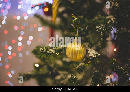 Nahaufnahme einer gelben Kugel, die an einem geschmückten Weihnachtsbaum hängt. Retro-Filtereffekt. Stockfoto