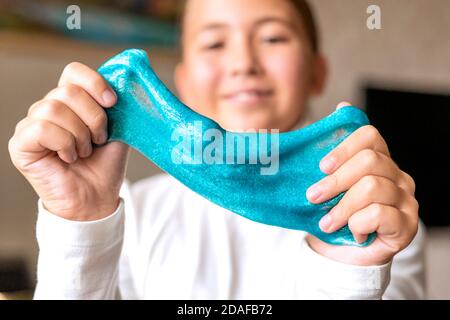 Mädchen Stretching blauen Glitzer Schleim an den Seiten. Kinder Hände spielen Schleim Spielzeug. Schleim machen. Konzentrieren Sie sich auf Schleim und Mädchen Hände. Geringe Schärfentiefe. Stockfoto